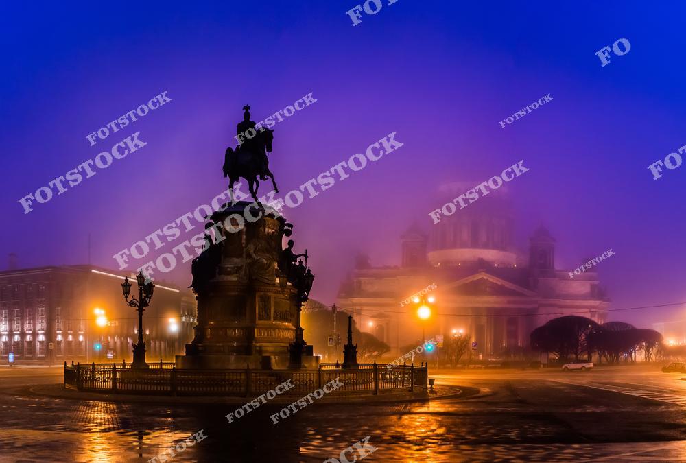 Атмосферный ночной Санкт-Петербург, окутанный густым туманом, с величественным памятником Петру I на Исаакиевской площади. Мягкий свет фонарей, отражения на мокрой мостовой и силуэты исторической архитектуры создают загадочный и романтичный городской пейзаж северной столицы России. Фотография передаёт уникальное настроение вечернего Петербурга, красоту его исторического центра и атмосферу старинного европейского города. Изображение идеально подходит для публикаций о Санкт-Петербурге, ночной архитектуре, путешествиях по России, туристических достопримечательностях и атмосферных городских сценах.